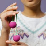 Close-up of a person holding purple kegel balls, illustrating pelvic floor trainer options for guide on trainers and apps.
