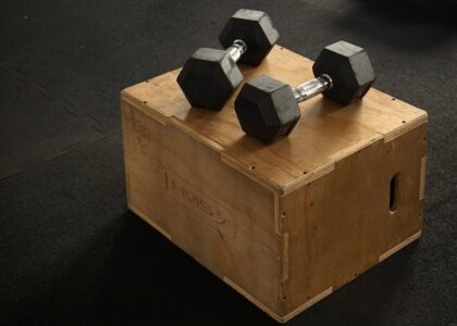 Pair of hex dumbbells on a wooden plyo box in a gym setting.