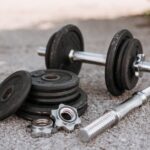Adjustable dumbbells with metal handles and loose weight plates on pavement, illustrating options for home strength training.