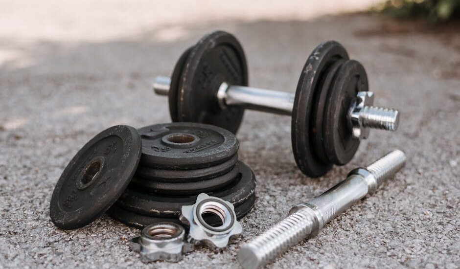 Adjustable dumbbells with metal handles and loose weight plates on pavement, illustrating options for home strength training.