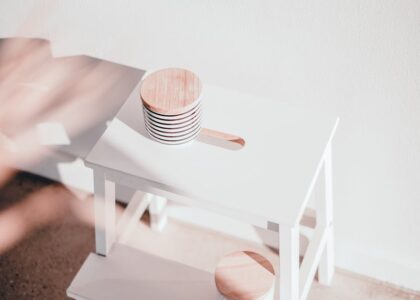A white wooden step stool with circular toppers bathed in natural sunlight, casting shadows.