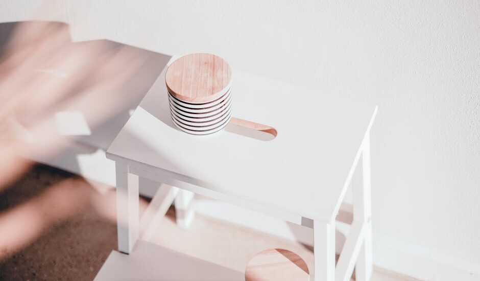 A white wooden step stool with circular toppers bathed in natural sunlight, casting shadows.