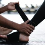Close-up of a person wrapping an ankle brace on another's foot next to someone wearing a compression sock, illustrating ankle support options.