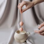 Person holding a pink pelvic floor trainer above a ceramic cup, illustrating the type of device discussed in pelvic floor health articles.