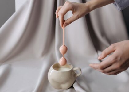 Person holding a pink pelvic floor trainer above a ceramic cup, illustrating the type of device discussed in pelvic floor health articles.