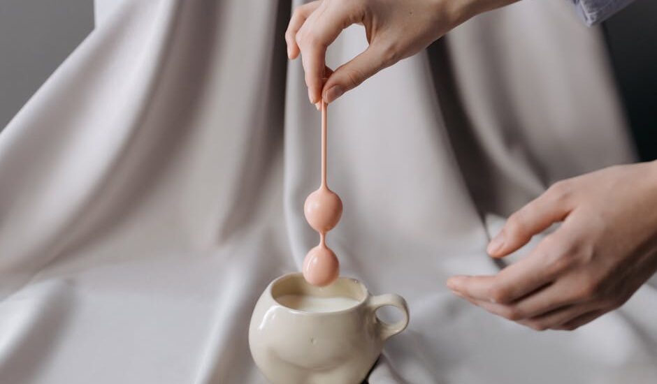 Person holding a pink pelvic floor trainer above a ceramic cup, illustrating the type of device discussed in pelvic floor health articles.