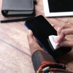 Person wiping a smartphone screen with a cloth, illustrating phone hygiene for the UV phone sanitizer evidence article