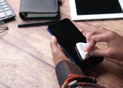 Person wiping a smartphone screen with a cloth, illustrating phone hygiene for the UV phone sanitizer evidence article