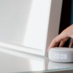 A hand adjusting a white noise machine on a table, relevant to white noise machines.