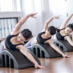 Three women in athletic wear demonstrate side stretches on foam back stretcher devices in a bright exercise studio, illustrating effective options for back reli