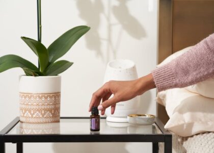 A hand reaches for a bottle of essential oil beside a white aromatherapy diffuser on a bedside table, illustrating sleep support.