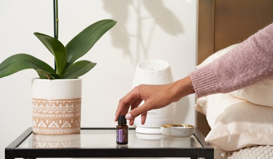 A hand reaches for a bottle of essential oil beside a white aromatherapy diffuser on a bedside table, illustrating sleep support.