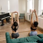 Two women practicing yoga indoors by a grand piano in a cozy living room with natural light.