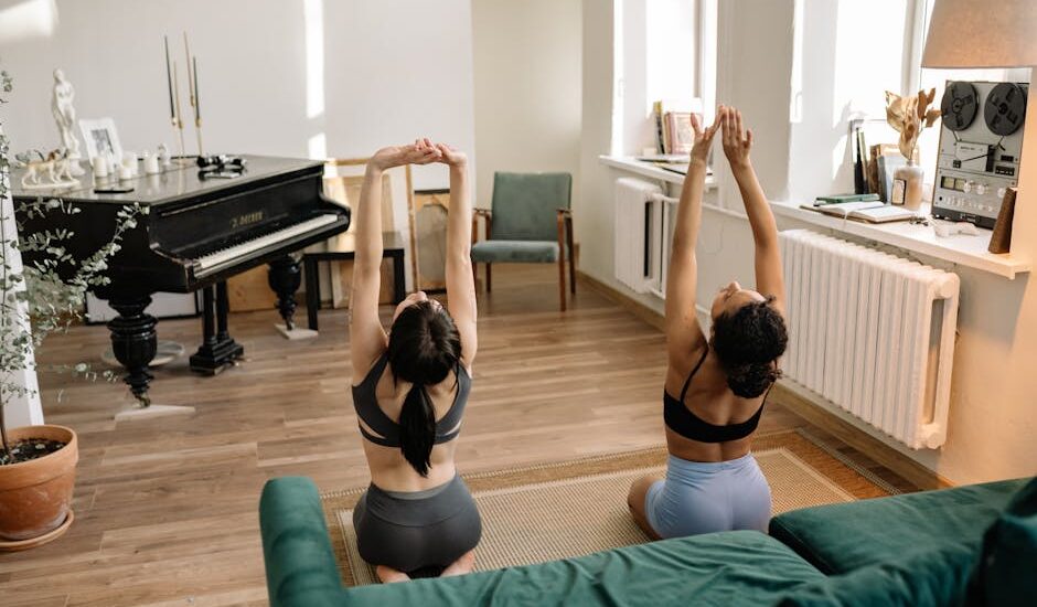 Two women practicing yoga indoors by a grand piano in a cozy living room with natural light.