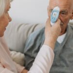 An elderly woman checks the temperature of a senior man using a digital thermometer indoors.