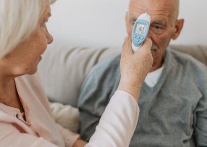 A person uses a digital forehead thermometer to measure an older man's body temperature, illustrating body temperature monitor use for the 2026 guide.