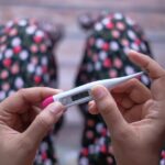 Close-up of hands holding a digital thermometer against a blurred background.