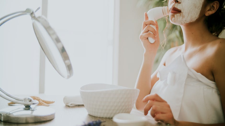 Person applies a facial mask and uses an electric cleansing brush, illustrating modern skincare routines for facial care.