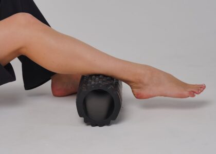 best electric foam roller — Close-up of a leg using a foam roller for stretching and muscle relief in a studio setting.