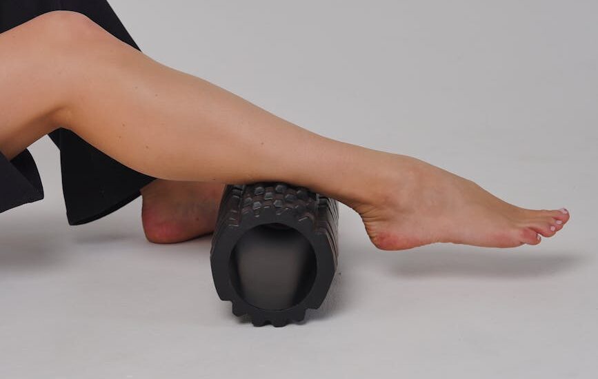 best electric foam roller — Close-up of a leg using a foam roller for stretching and muscle relief in a studio setting.