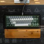A compact ergonomic keyboard with green and white keys and a wooden wrist rest, shown on a desk for a 2026 ergonomic keyboard guide.