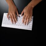 Overhead view of hands typing on a sleek white keyboard on dark surface.