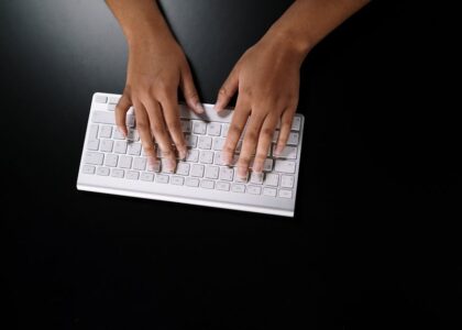Overhead view of hands typing on a sleek white keyboard on dark surface.