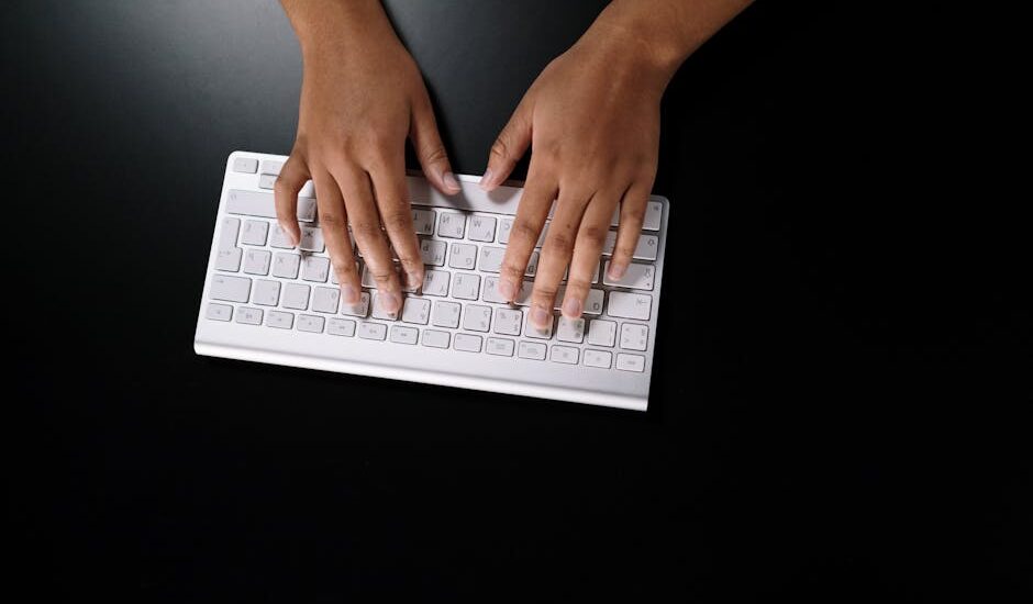 Overhead view of hands typing on a sleek white keyboard on dark surface.