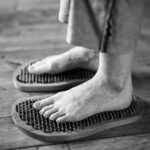 Black and white photo of feet receiving a relaxing massage on wooden reflexology boards.