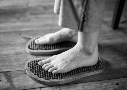 Black and white photo of feet receiving a relaxing massage on wooden reflexology boards.