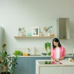 Asian woman chopping vegetables on a kitchen counter in a stylish, modern kitchen setting.