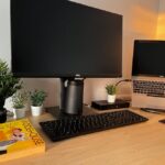 A modern home office setup featuring a monitor, laptop, and greenery for remote work inspiration.