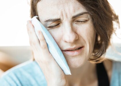 A woman in discomfort applying a cold compress to her cheek for relief from toothache pain.