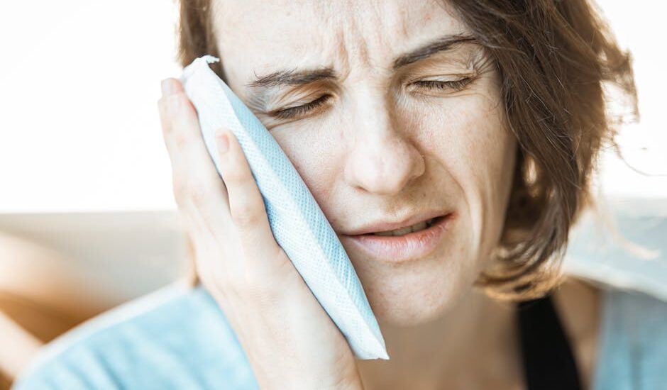 A woman in discomfort applying a cold compress to her cheek for relief from toothache pain.