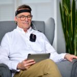 Man sits in an armchair using a tablet and wearing a headband-style mindfulness device, illustrating top mindfulness tech for 2026.