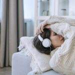 A young woman in a knitted sweater relaxing with headphones, conveying a sense of calm and introspection.