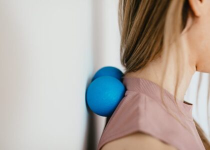 A person uses two blue massage balls against a wall for neck relief, illustrating a technique featured in the best neck massagers 2026 guide.