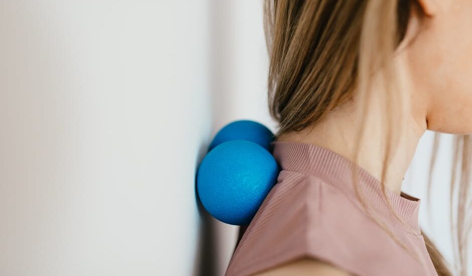 A person uses two blue massage balls against a wall for neck relief, illustrating a technique featured in the best neck massagers 2026 guide.