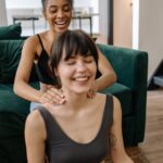 Two women enjoy a relaxing neck massage at home, highlighting friendship and wellness.