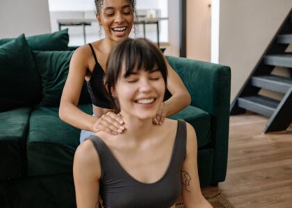 Two women enjoy a relaxing neck massage at home, highlighting friendship and wellness.