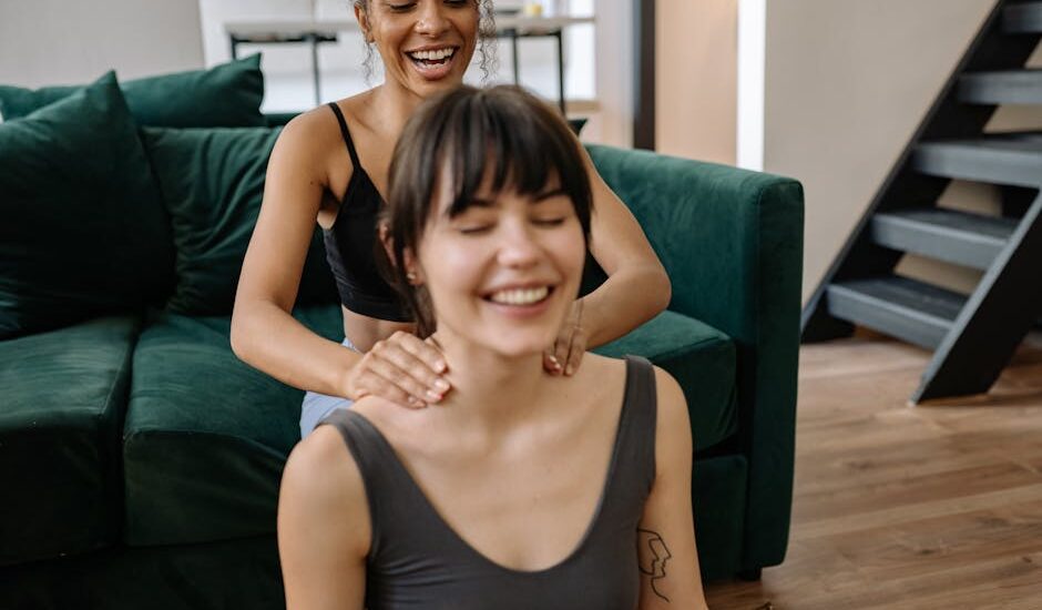 Two women enjoy a relaxing neck massage at home, highlighting friendship and wellness.