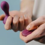 Close-up of a man’s hands holding a purple pelvic floor trainer and its matching remote, illustrating men’s pelvic health devices.