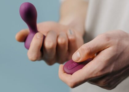 Close-up of a man’s hands holding a purple pelvic floor trainer and its matching remote, illustrating men’s pelvic health devices.
