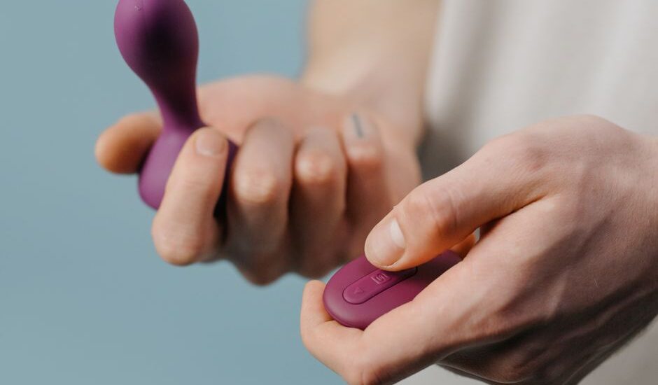Close-up of a man’s hands holding a purple pelvic floor trainer and its matching remote, illustrating men’s pelvic health devices.