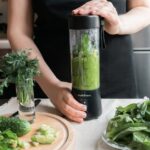 A person making a healthy green smoothie with fresh vegetables in a modern kitchen.