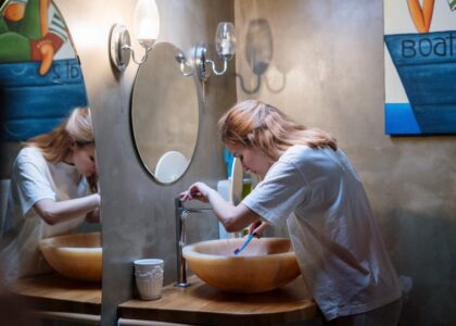 A woman brushing her teeth in a cozy, modern bathroom with warm lighting and artistic decor.