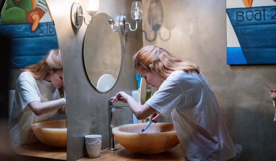 A woman brushing her teeth in a cozy, modern bathroom with warm lighting and artistic decor.
