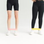 Two women in activewear using resistance bands during an indoor workout session.