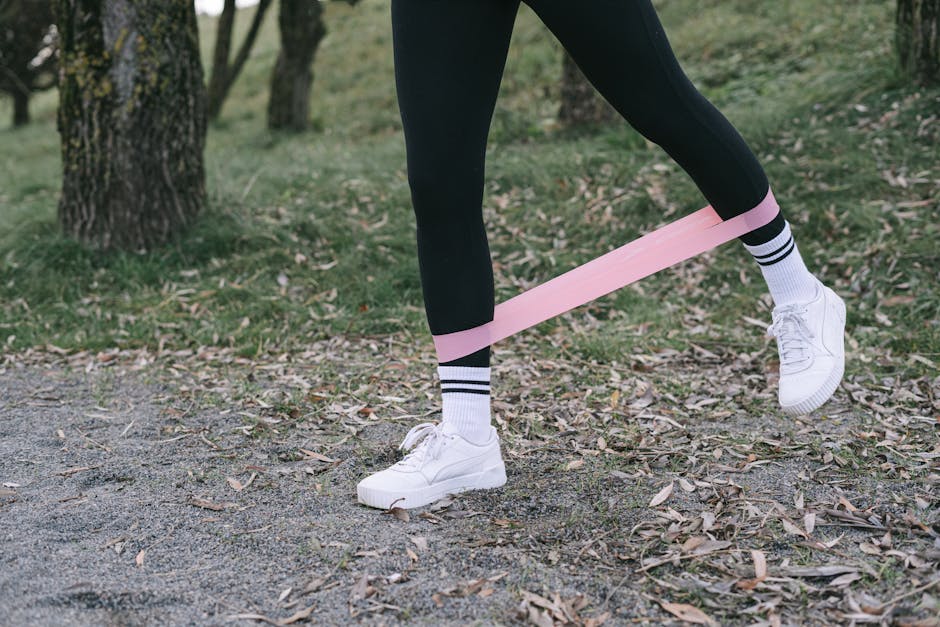 Close-up of person exercising with a pink resistance band outdoors.