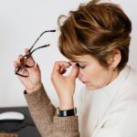 Woman feeling stressed and tired at work, holding eyeglasses with eyes closed.